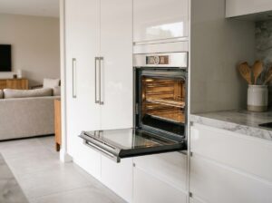 Four encastrable moderne intégré dans une cuisine blanche contemporaine avec porte en inox légèrement ouverte