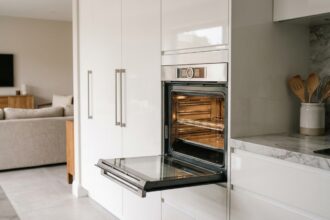 Four encastrable moderne intégré dans une cuisine blanche contemporaine avec porte en inox légèrement ouverte